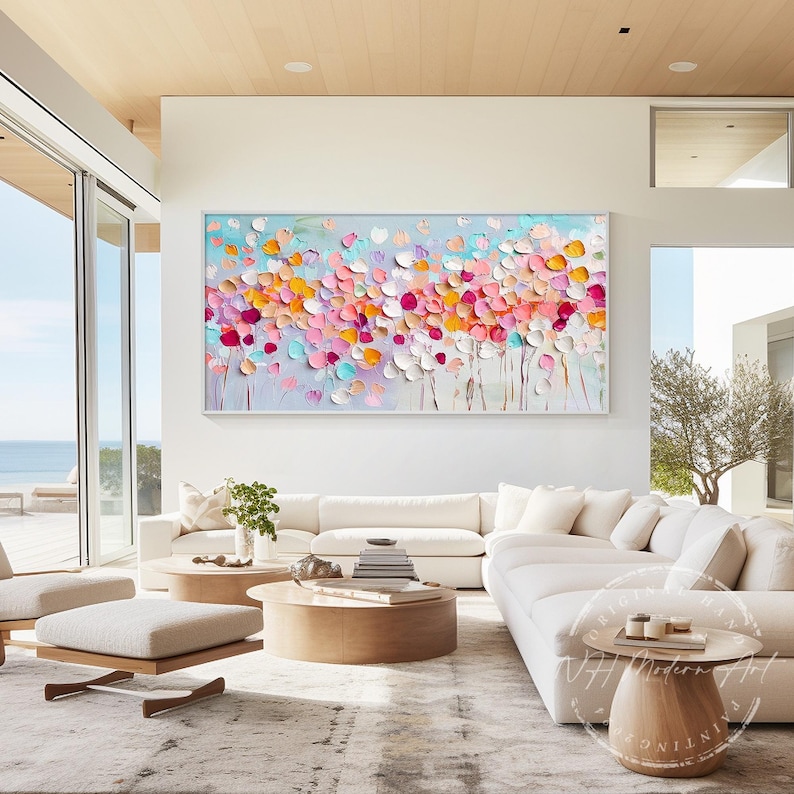 May include: A large abstract painting with a white background and colorful flowers in shades of pink, orange, yellow, and blue. The painting is hanging on a white wall in a modern living room.