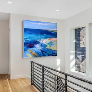 May include: Abstract painting of a seascape with blue, green, white, and yellow hues. The painting is framed and hanging on a white wall in a modern home.
