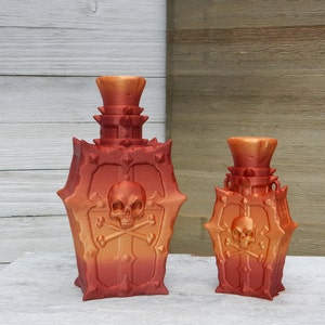 Könnte beinhalten: Zwei dekorative Glasflaschen mit einem Totenkopf- und Knochenkreuz-Design. Die Flaschen sind in einem Farbverlauf von Orange und Rot.
