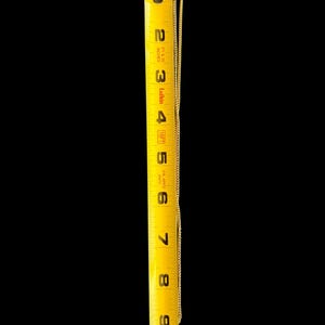 Peut inclure: Un collier dor&eacute; avec un pendentif, mesur&eacute; contre un m&egrave;tre ruban jaune. La cha&icirc;ne s'&eacute;tend sur environ 20 cm. Le pendentif a un centre sombre avec une bordure dor&eacute;e d&eacute;corative. Le fond est noir.