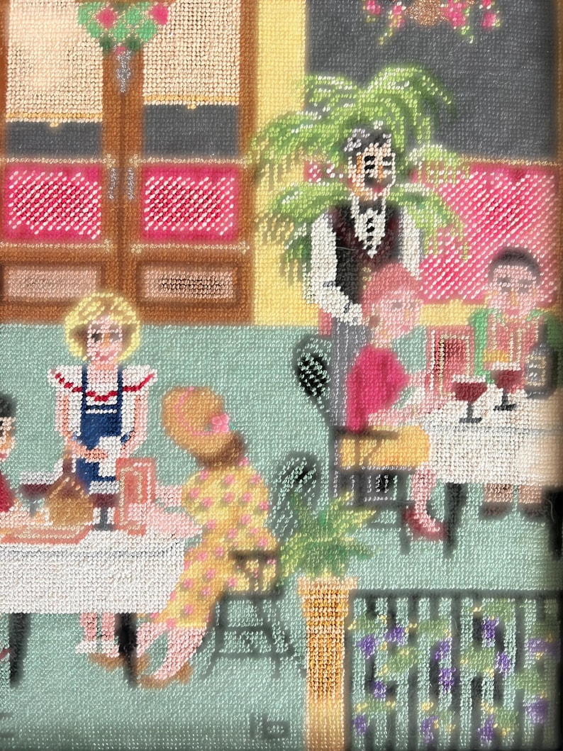 May include: Needlepoint artwork depicting a restaurant scene. The image shows people seated at tables, with a waiter in the background. The color palette includes pink, yellow, and green, with a textured appearance. The artwork has a vintage aesthetic.
