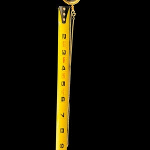 Peut inclure: Un collier dor&eacute; avec un pendentif ovale noir orn&eacute; d'un motif floral dor&eacute;. Le pendentif mesure environ 5 cm de long. La cha&icirc;ne du collier est d&eacute;licate et descend le long du ruban &agrave; mesurer.