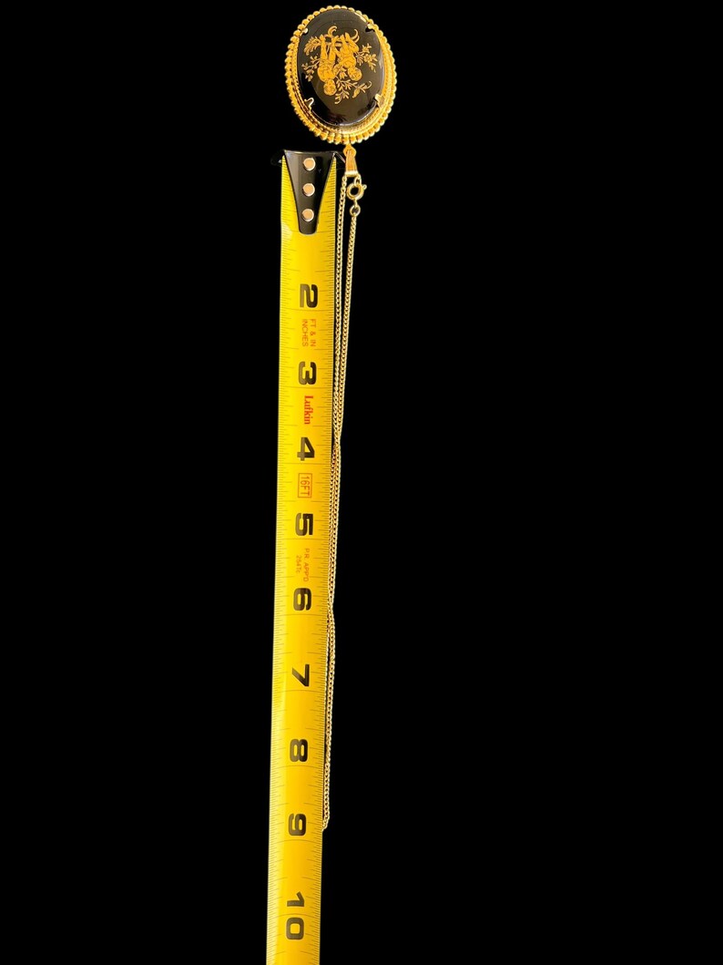 Peut inclure: Un collier dor&eacute; avec un pendentif ovale noir orn&eacute; d'un motif floral dor&eacute;. Le pendentif mesure environ 5 cm de long. La cha&icirc;ne du collier est d&eacute;licate et descend le long du ruban &agrave; mesurer.