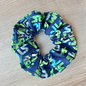 May include: A dark blue scrunchie with a green and white pattern of letters and small green alien-like figures.
