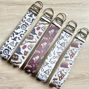 May include: Six white leather keychains with different Harry Potter themed designs. The keychains feature images of owls, potions, wands, and the Hogwarts crest.