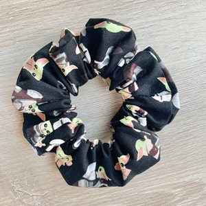 May include: Black scrunchie with a repeating pattern of green, yellow, and white cartoon characters.