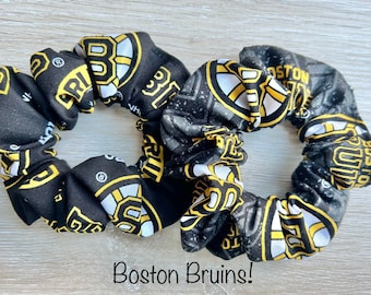 Puede incluir: Dos scrunchies negros y dorados con el logotipo de los Boston Bruins. Los scrunchies están hechos de tela y tienen una superficie texturizada.