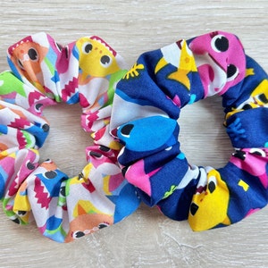 Pu&ograve; includere: Due scrunchies per capelli colorati con un motivo di baby shark. Uno scrunchie &egrave; bianco con baby shark rosa, blu, giallo e verde. L'altro scrunchie &egrave; blu navy con baby shark rosa, giallo e blu.