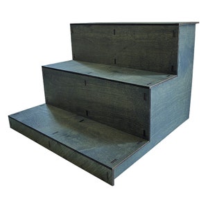 May include: A three-tiered, dark gray wooden display stand. The stand has a stepped design, with each level slightly smaller than the one below. The wood grain is visible, and the edges are cleanly cut. Ideal for showcasing products.