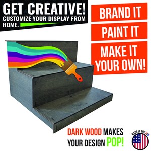 May include: A dark gray, three-tiered display stand with a rainbow paint stroke and a paintbrush. Text reads "Get Creative! Customize Your Display From Home." and "Brand It, Paint It, Make It Your Own!" The stand is made in the USA.