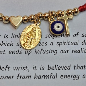 Puede incluir: Pulsera de hilo rojo con cuentas y dijes dorados. Los dijes incluyen un coraz&oacute;n, una cruz, un ojo y un medall&oacute;n con la imagen de una persona. La pulsera est&aacute; vinculada a una secuencia de siete.
