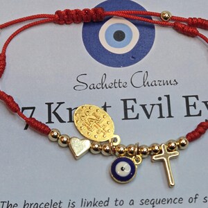 Puede incluir: Pulsera de hilo rojo con cuentas y dijes dorados, incluyendo un coraz&oacute;n, una cruz y un ojo turco. La pulsera tiene un cierre de nudo corredizo. El texto "Sachette Charms" y "7 Knot Evil Eye" son visibles.