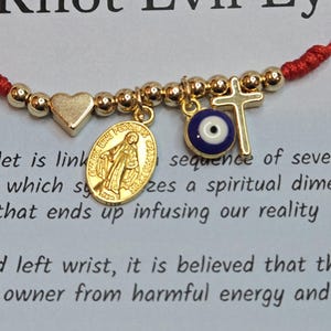 Puede incluir: Pulsera de cord&oacute;n rojo con dijes dorados: un coraz&oacute;n, una medalla religiosa, una cruz y un ojo turco. La pulsera est&aacute; vinculada a una secuencia de siete nudos.