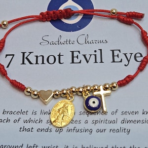 Puede incluir: Pulsera de hilo rojo con cuentas y dijes dorados. Los dijes incluyen un coraz&oacute;n, una cruz, un medall&oacute;n y un ojo turco. El texto en la tarjeta dice "7 Knot Evil Eye".
