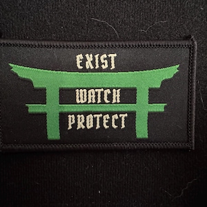 Puede incluir: Parche rectangular negro con texto y diseño bordados en verde y blanco. El texto dice "EXIST WATCH PROTECT" encima y debajo de un diseño de puerta estilizada verde. El parche es probablemente para ropa o accesorios.