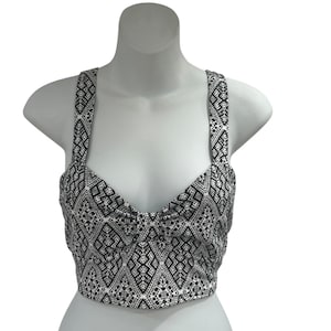 May include: A black and white patterned crop top with thick straps. The top features a geometric design and is displayed on a white mannequin. The fabric has a repeating pattern of small shapes.