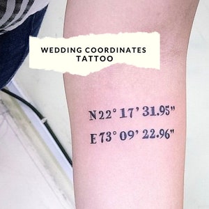 May include: A close-up of a person's arm with a tattoo that reads "WEDDING COORDINATES TATTOO" and the coordinates "N22° 17' 31.95" and "E73° 09' 22.96".