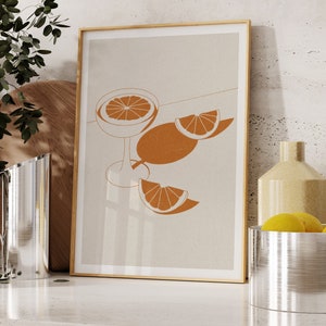Peut inclure: Une impression encadr&eacute;e avec un design minimaliste repr&eacute;sentant un verre de jus d'orange et des tranches d'orange sur un fond beige.