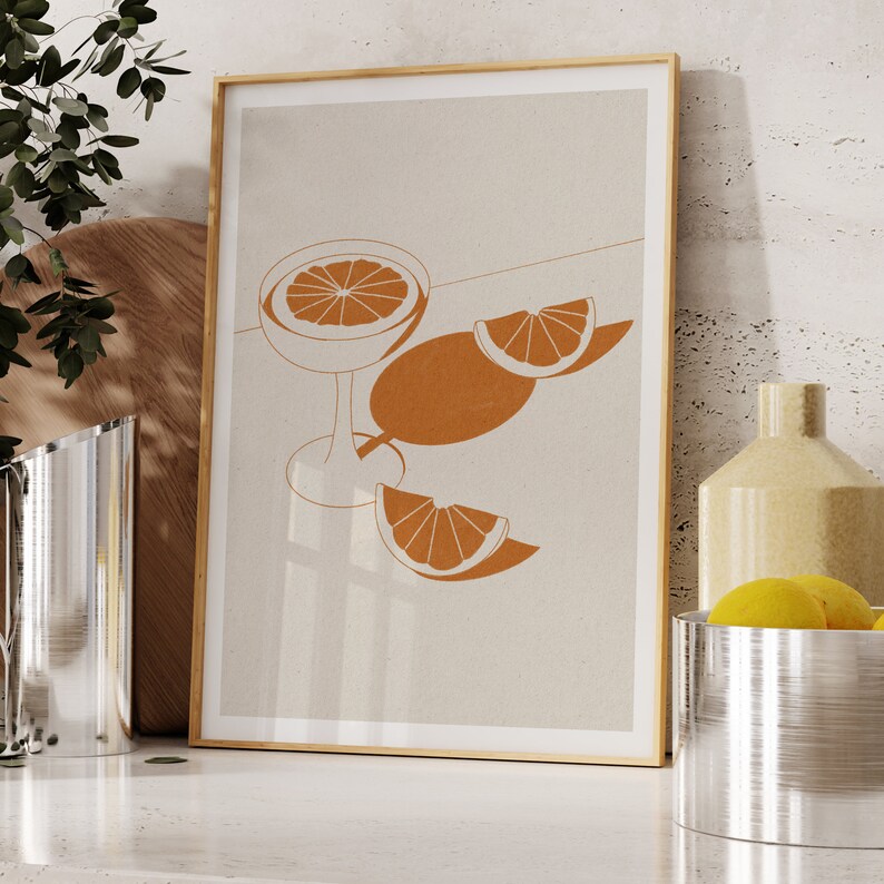 Peut inclure: Une impression encadr&eacute;e avec un design minimaliste repr&eacute;sentant un verre de jus d'orange et des tranches d'orange sur un fond beige.