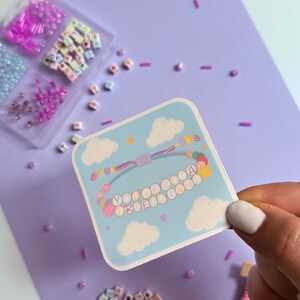 May include: A square sticker featuring a light blue sky background with white clouds and a colorful beaded bracelet illustration. The bracelet has letter beads spelling out the phrase YOU'VE GOT A FRIEND IN ME, accented with small hearts and stars.