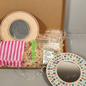 May include: A craft kit for making a mosaic mirror. The kit includes a wooden base with a pre-cut mosaic design, a small bag of colourful tiles, a small bag of adhesive, and a small green tool. The kit also includes instructions for assembly.