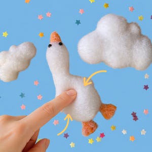 May include: A white felt goose with an orange beak and feet, set against a blue background with white cloud shapes and colorful star confetti. The goose is being touched by a finger.