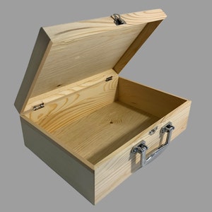 May include: A light-colored wooden box with the lid slightly open. The box has a rectangular shape with a hinged lid and a metal clasp closure. A metal handle is attached to the front. The wood grain is visible.