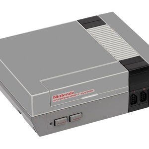 Pode incluir: Um console cinza do Nintendo Entertainment System com uma ranhura de cartucho preta e duas portas de controle. O console tem um design cinza e preto com o texto "Nintendo Entertainment System" impresso em vermelho.