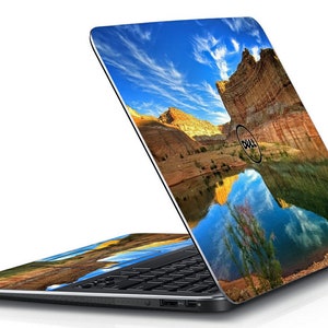 May include: A black Dell laptop with a colourful landscape image on the lid. The image shows a canyon with a lake reflecting the sky and clouds. The Dell logo is visible on the lid.