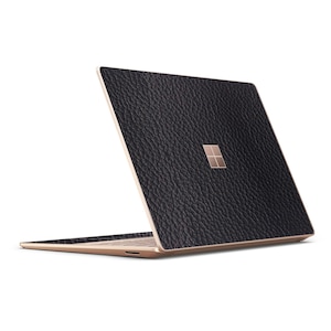 May include: A black laptop with a textured leather-like finish. The laptop has a rose gold colored frame and a Microsoft logo on the lid.