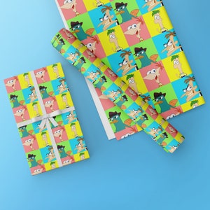 May include: Two rolls of wrapping paper featuring a repeating pattern of cartoon characters from the animated series Phineas and Ferb. The characters are in a pop art style with bright yellow, blue, pink, and green colors.