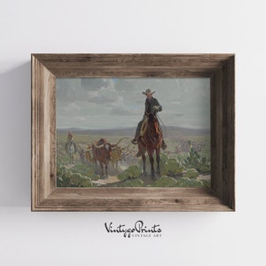 May include: A vintage painting depicting a cowboy on horseback leading a herd of cattle across a dusty landscape. The cowboy is wearing a hat and a long coat, and the cattle are brown and white. The painting is framed in a wooden frame.
