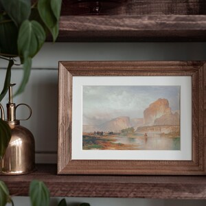 May include: A framed landscape painting depicting a river flowing through a canyon with a mountain in the background. The painting is in a rustic wooden frame.