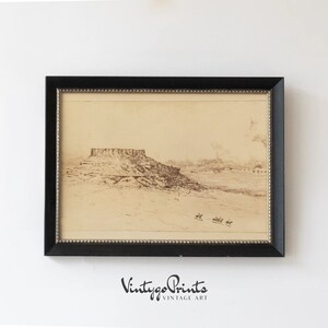 May include: A vintage black and white print of a landscape with a large rock formation in the distance. The print is framed in a black frame with a gold trim.
