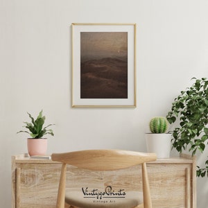 Puede incluir: Una impresi&oacute;n enmarcada de un paisaje con una cordillera en la distancia. El cielo es de un naranja apagado y las monta&ntilde;as son de un marr&oacute;n oscuro. La impresi&oacute;n est&aacute; en un marco dorado y est&aacute; colgada en una pared blanca.