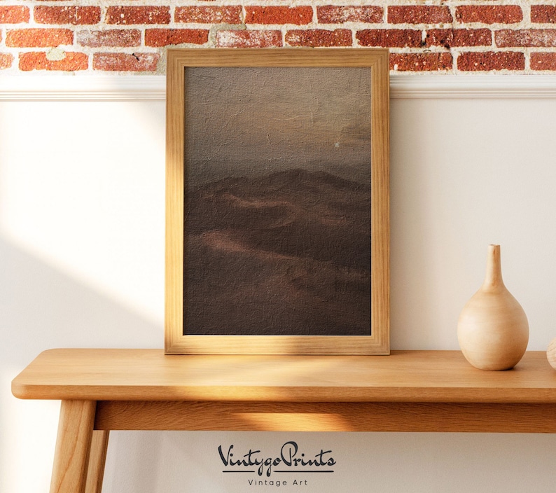 Puede incluir: Una pintura de paisaje enmarcada que representa una cordillera marr&oacute;n y gris bajo un cielo nublado. La pintura est&aacute; en un marco de madera con un acabado marr&oacute;n claro.