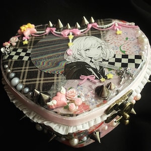 May include: Heart-shaped box with a collage design. The box features a black and white anime illustration, plaid and floral patterns, and decorative elements like spikes, bows, and pearls. The text "A void within" is visible.