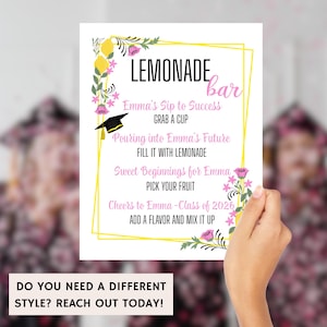 K&ouml;nnte beinhalten: Ein wei&szlig;es Schild mit dem Text "LEMONADE bar" in Schwarz und Rosa, verziert mit Blumen- und Zitronenmotiven. Das Schild enth&auml;lt S&auml;tze wie "Emma's Sip to Success" und "Cheers to Emma - Class of 2026". Unten steht "DO YOU NEED A DIFFERENT STYLE? REACH OUT TODAY!"