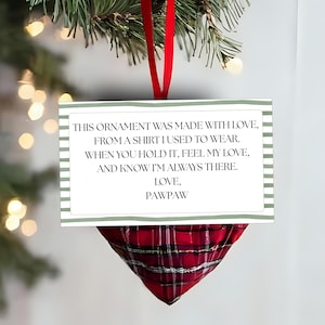 Könnte beinhalten: Weihnachtsschmuck mit roter karierter Stoffbasis und einer rechteckigen Karte. Die Karte hat einen grün-weiß gestreiften Rand und lautet: "THIS ORNAMENT WAS MADE WITH LOVE, FROM A SHIRT I USED TO WEAR... LOVE, PAWPAW."