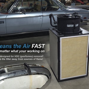 May include: A black air purifier with a large fan and a yellow filter. The text "CATERP LAR" is visible on the front of the purifier. The text "Cleans the Air FAST" is visible in the image. The text "No matter what your working on" is visible in the image. The text "Not designed for VOC (gas/fumes) removal!" is visible in the image. The text "Keep the filter away from sources of flame!" is visible in the image.