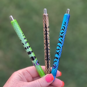 May include: Three colorful pens with different animal print designs. The pens are green, blue, and brown with black accents. The pens have a silver top.