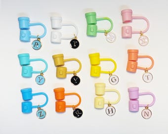May include: A collection of colorful, plastic earbud holders in various shades, including blue, white, green, and pink. Each holder has a unique charm with a letter. The holders are designed to keep earbuds organized and tangle-free.