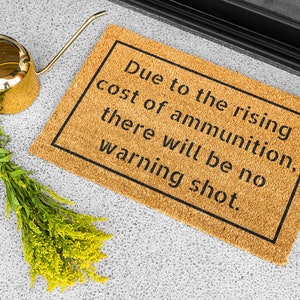 May include: A brown coir doormat with the text "Due to the rising cost of ammunition, there will be no warning shot." printed in black.