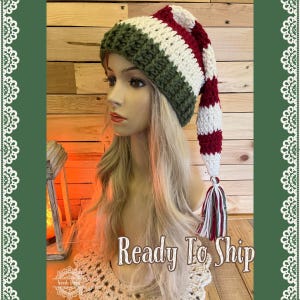 May include: A white, green, and red striped crochet hat with a long, pointed tail and a tassel. The hat is ready to ship.