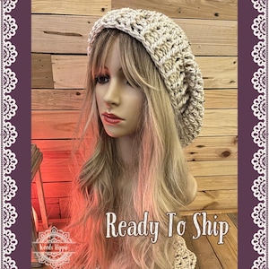 Peut inclure: Un béret en crochet beige avec une coupe ample. Le béret est sur un mannequin avec de longs cheveux blonds. Le texte "Ready To Ship" est visible sur l'image.