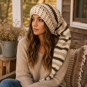 May include: A long, slouchy crochet beanie featuring a thick, ribbed knit texture with alternating horizontal stripes in cream and dark brown. The hat has a tapered, extended tail design that hangs down to one side, crafted from chunky yarn.
