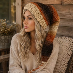 May include: A long, slouchy crochet beanie featuring a gradient color pattern that transitions from cream at the brim to shades of orange, rust, and dark brown. The hat has a textured, chunky knit construction and a long, pointed tail that hangs down.