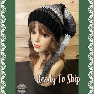 Puede incluir: Un gorro de ganchillo hecho a mano en rayas negras, grises y blancas. El gorro tiene un extremo largo y puntiagudo. El texto "Ready To Ship" se muestra en la imagen. El gorro se muestra en una cabeza de maniquí.