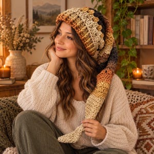 May include: A long, slouchy crochet beanie featuring a gradient color pattern that transitions from cream and tan to warm orange, brown, and dark charcoal. The hat is crafted with a textured stitch pattern and has a tapered, elongated tail design.