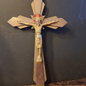 Op de afbeelding: Een vintage kruisbeeld met een goudkleurige Jezusfiguur op een houten kruis. Het kruis heeft een decoratief ontwerp met een rode cirkel in het midden. De figuur is gedetailleerd, met uitgestrekte armen.
